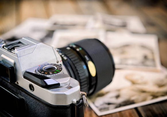 Close up of vintage photographic prints, film camera and on a rustic wooden table.